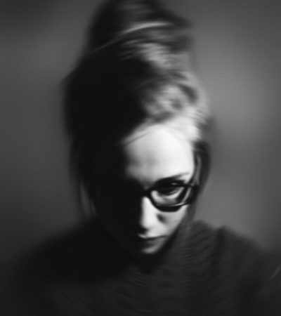 Grayscale portrait of a woman with glasses, exhibiting a pensive mood in studio lighting.