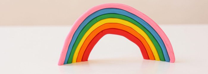 A vibrant clay rainbow sculpture on a white background, showcasing a minimalistic art piece.
